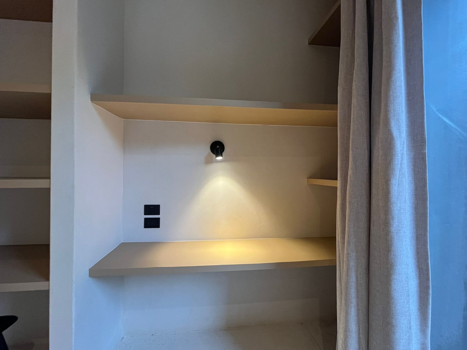 A modern interior with a staircase, a wall-mounted light fixture, and a door with a curtain.