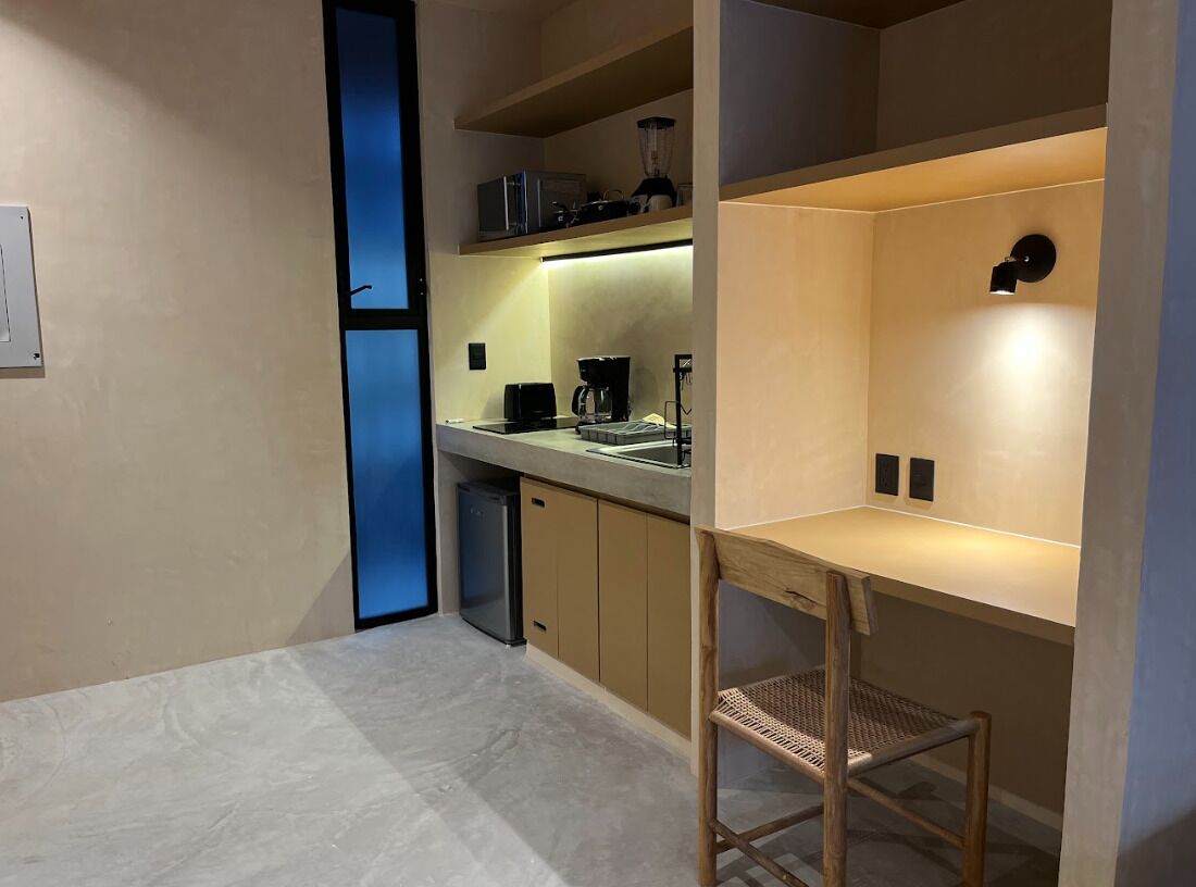 A compact kitchen with a built-in coffee machine, a sink, and a small stool.