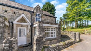 A stone building with a white door and window, surrounded by a stone wall and greenery. - 2 Bed in Trewoon (oc-t29503) (Saint Mewan)