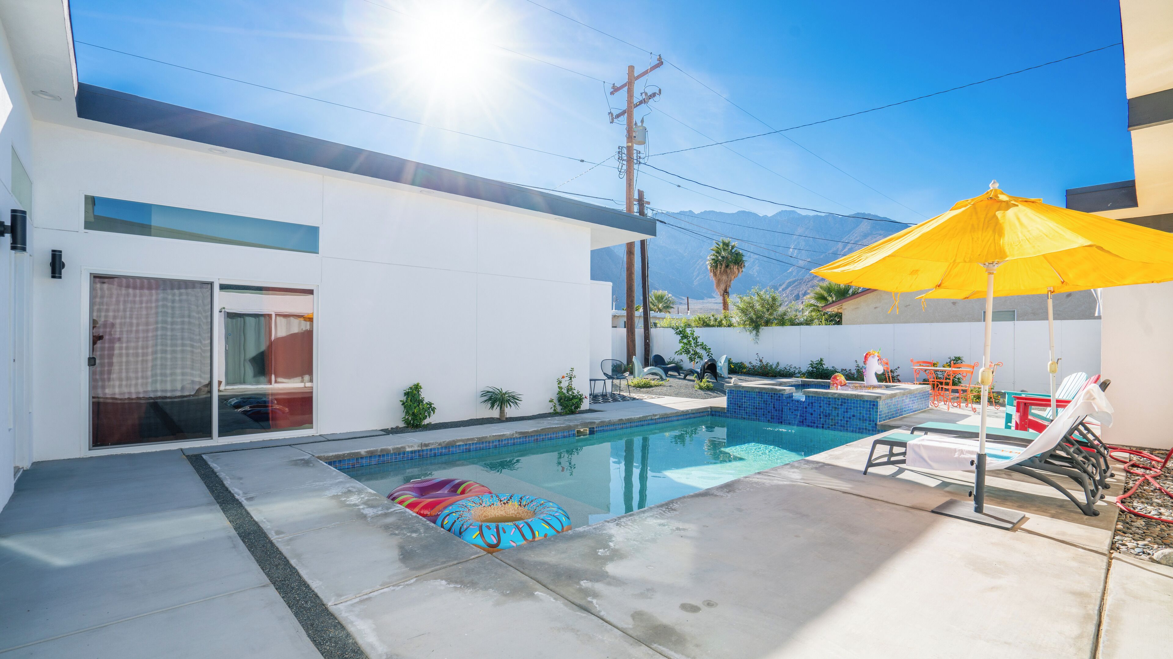 A modern outdoor pool area with a clear blue sky, a yellow umbrella, and lounge chairs.