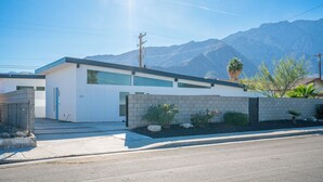 Una casa moderna de dos pisos con fachada blanca, una puerta azul y el número "473" en la pared.