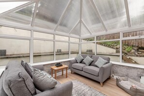 A conservatory with a grey sofa, patterned cushions, a small table, and a pet bed. - 2 Bed in Wooler (oc-l29429) (Wooler)