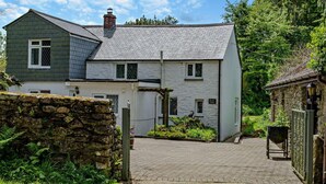 A two-story house with a stone wall entrance, a paved driveway, and a garden area with plants and a stone wall.