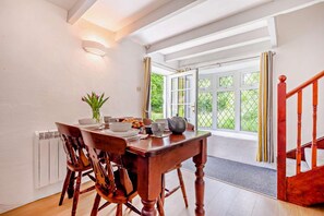 Un coin repas avec une table et des chaises en bois, un vase de fleurs et une vue sur l’extérieur grâce à de grandes fenêtres.