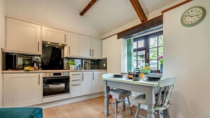 A modern kitchen with white cabinets, a dining table, and chairs. There is a window with a view of greenery outside. - 1 Bed in Advent (oc-b29387) (Advent)