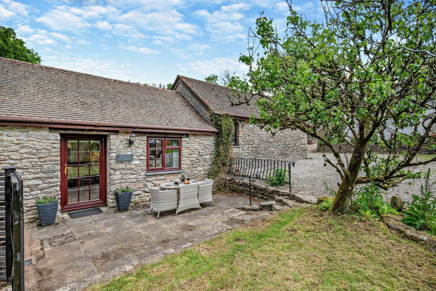 A stone cottage with a tiled roof, a front door, and a small outdoor seating area with a table and chairs.