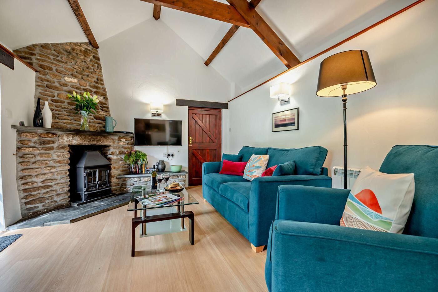 A cozy living room with a stone fireplace, a blue sofa set, a glass coffee table, and a floor lamp.