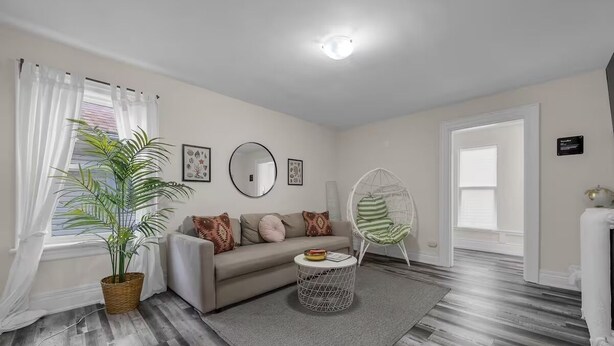Ein Wohnzimmer mit einer Couch, einem runden Couchtisch, einer Zimmerpflanze, einem Sessel und einem großen Spiegel an der Wand.