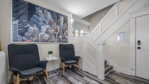 Ein modernes Interieur mit zwei dunklen Stühlen, einem Stadtbildgemälde, einem kleinen Tisch mit einer Pflanze und einer Treppe, die zu einer Tür führt.