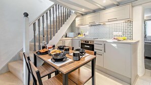 A modern kitchen with a wooden dining table set for breakfast, a staircase, and a tiled backsplash. - 2 Bed in Advent (oc-p6188) (Advent)