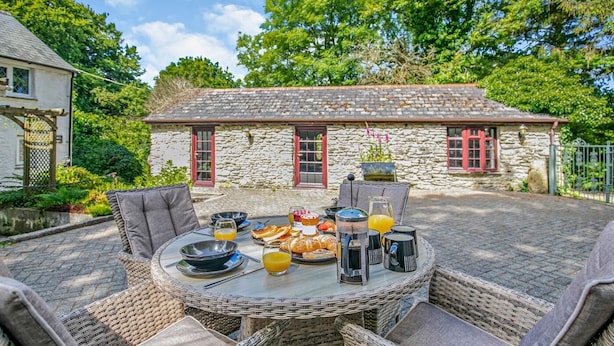 An outdoor dining area with wicker furniture, a stone building with red windows in the background, and a variety of breakfast items on the table. - 2 Bed in Advent (oc-p6188) (Advent)