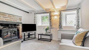 A cozy living room with a stone fireplace, a flat-screen TV, a grey sofa, and a window with patterned curtains. - 2 Bed in Advent (oc-p6188) (Advent)