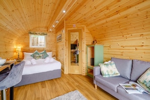 Una stanza accogliente di una casetta in legno con un letto, una divano, una scrivania e un armadietto verde.