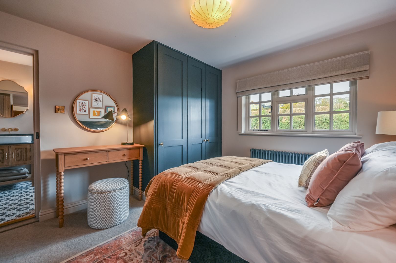 A bedroom with a bed, a desk, a wardrobe, a window with a view, and a radiator.