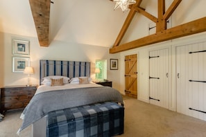 Ein Schlafzimmer mit einem großen Bett, einer hölzernen Bank, einem Nachttisch, einer Lampe und einem Kleiderschrank mit schwarzen Griffen.
