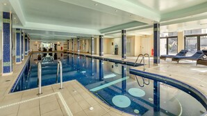 Una piscina interior con agua cristalina, rodeada de sillones de descanso y un suelo de baldosas.