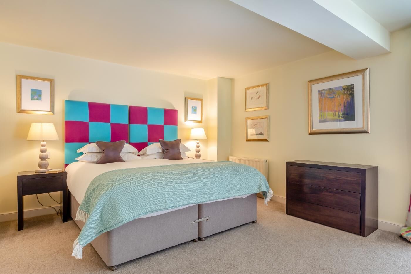 A bedroom with a bed, bedside tables, a dresser, and framed artwork on the walls.