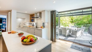 Uma cozinha moderna com uma ilha grande, área de jantar com assentos externos e vista para um jardim exuberante.