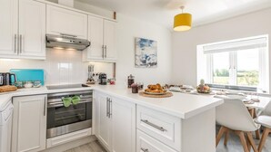 A modern kitchen with white cabinetry, a built-in oven, and a dining area with a view. - 2 Bed in St. Minver (oc-r29475) (Saint Minver)