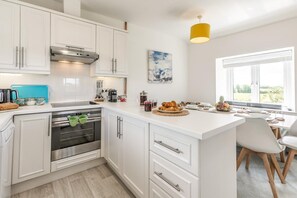 A modern kitchen with white cabinetry, a built-in oven, and a dining area with a view. - 2 Bed in St. Minver (oc-r29475) (Saint Minver)