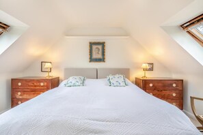 A bedroom with a large bed, two nightstands, a framed picture on the wall, and a skylight.