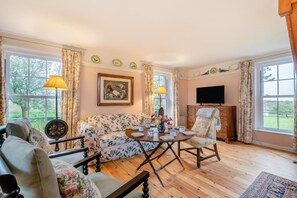 A cozy living room with a floral sofa, a wooden coffee table, and a television on the wall.