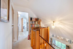 Una escalera con barandilla de madera, una estantería y un candelabro.