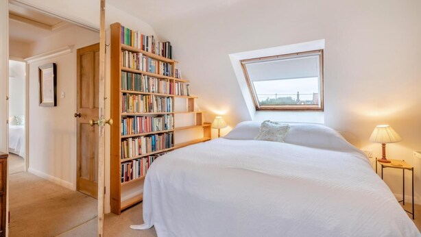 A bedroom with a large bed, a bookshelf, a skylight, and a door leading to another room. - 5 Bed in Morston (oc-s29448) (Morston)