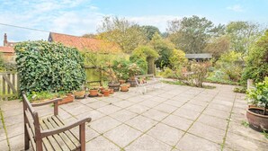 A garden patio with a wooden bench, potted plants, and a tiled floor. - 5 Bed in Morston (oc-s29448) (Morston)