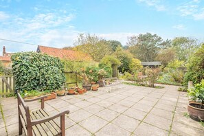 A garden patio with a wooden bench, potted plants, and a tiled floor. - 5 Bed in Morston (oc-s29448) (Morston)