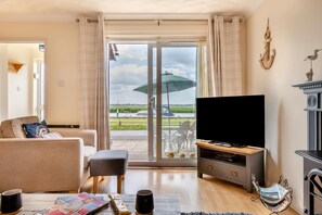A living room with a sofa, a television, and a view of a body of water through a glass door. - 2 Bed in Reedham (oc-c29528) (Haddiscoe)