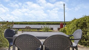 Ein Tisch mit zwei Stühlen, der auf einen Fluss ausgerichtet ist, mit einem roten Briefkasten und einer Bank im Hintergrund.