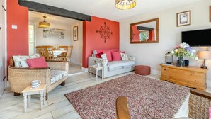 Ein gemütliches Wohnzimmer mit roter Akzentwand, einem weißen Sofa, Korbstühlen, einem Holztisch und einem großen Teppich.