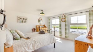 Ein Schlafzimmer mit Bett, Nachttisch, Kommode und einem Fenster mit Blick auf ein Gewässer.