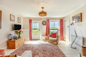 A spacious living room with a large window, a television, a wicker chair, and a red and white checkered curtain. - 2 Bed in Reedham (oc-q29527) (Haddiscoe)