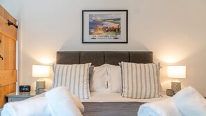 Una habitación de hotel con una cama, dos mesitas de noche, un cuadro enmarcado y un reloj digital.