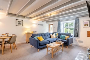 Ein modernes Wohnzimmer mit einem blauen Sofa, einem Holztisch und einem Essbereich mit Tisch und Stühlen.