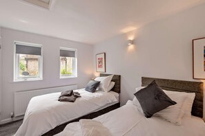 Ein Schlafzimmer mit zwei Betten, einem Heizkörper, Fenstern mit Jalousien und einem gerahmten Bild an der Wand.