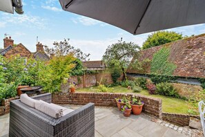 Eine Terrasse mit Gartenmöbeln, einer Backsteinmauer und Kübelpflanzen.
