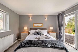 Une chambre à coucher avec un lit, deux tables de chevet avec des lampes, un radiateur, une fenêtre et une vue sur l’extérieur.