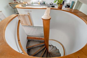 Eine Wendeltreppe mit Holzgeländern und Teppichstufen führt zu einer Küchenzeile mit modernen Geräten und einem Topfpflanzen.