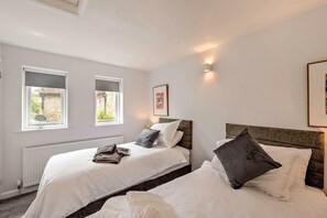 Ein Schlafzimmer mit zwei Betten, einem Heizkörper und zwei Fenstern mit Jalousien.