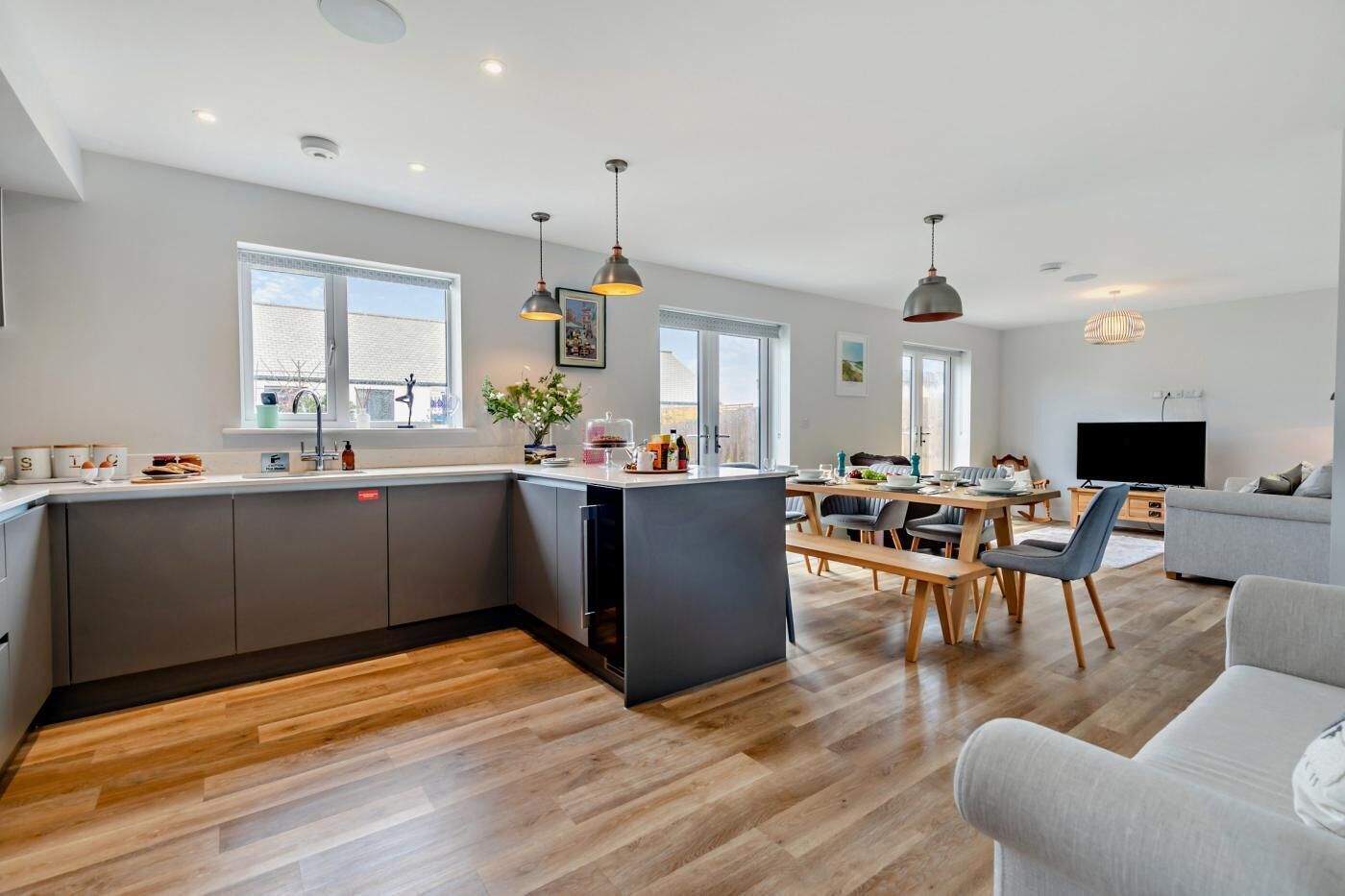 Eine moderne Küche mit Kochinsel, Essbereich mit Tisch und Stühlen, einer Couch und einem Fernseher im Wohnzimmer.
