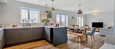 Een moderne keuken met een centraal kookeiland, een eethoek met tafel en stoelen, een bank en een televisie in een woonkamer.