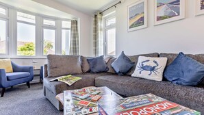 Ein Wohnzimmer mit grauem Sofa, blauem Sessel und einem Couchtisch mit Gesellschaftsspielen.