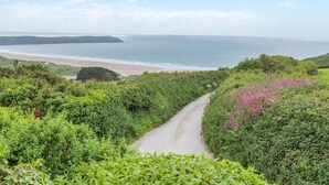A coastal road surrounded by lush greenery and a beach in the distance. - 4 Bed in Woolacombe (oc-t5715) (Woolacombe)
