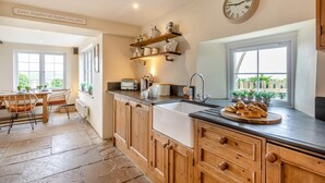 A kitchen with wooden cabinets, a sink, a toaster, and a clock on the wall. - 4 Bed in Woolacombe (oc-t5715) (Woolacombe)