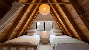 Ein gemütliches Schlafzimmer im Dachgeschoss mit zwei Betten, einem großen Fenster und einer Pendelleuchte.