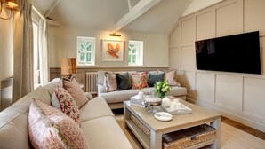 Ein geräumiges Wohnzimmer mit hoher Decke, einem großen Flachbildfernseher an der Wand, einer gemütlichen Sofagarnitur und einem Couchtisch mit Dekoration.