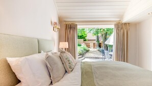 Ein Schlafzimmer mit einem Bett, zwei Nachttischlampen und Blick auf einen Garten sowie eine Sitzgelegenheit im Freien.